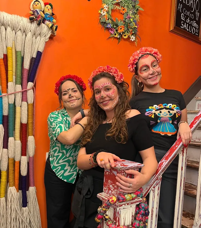 Three members of the restaurant team in Day of the Dead face paint and flower crowns, on the colourful staircase